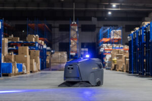 Robot quét hút bụi công nghiệp Gausium Beetle hoạt động trong nhà kho, giữa các kệ hàng pallet