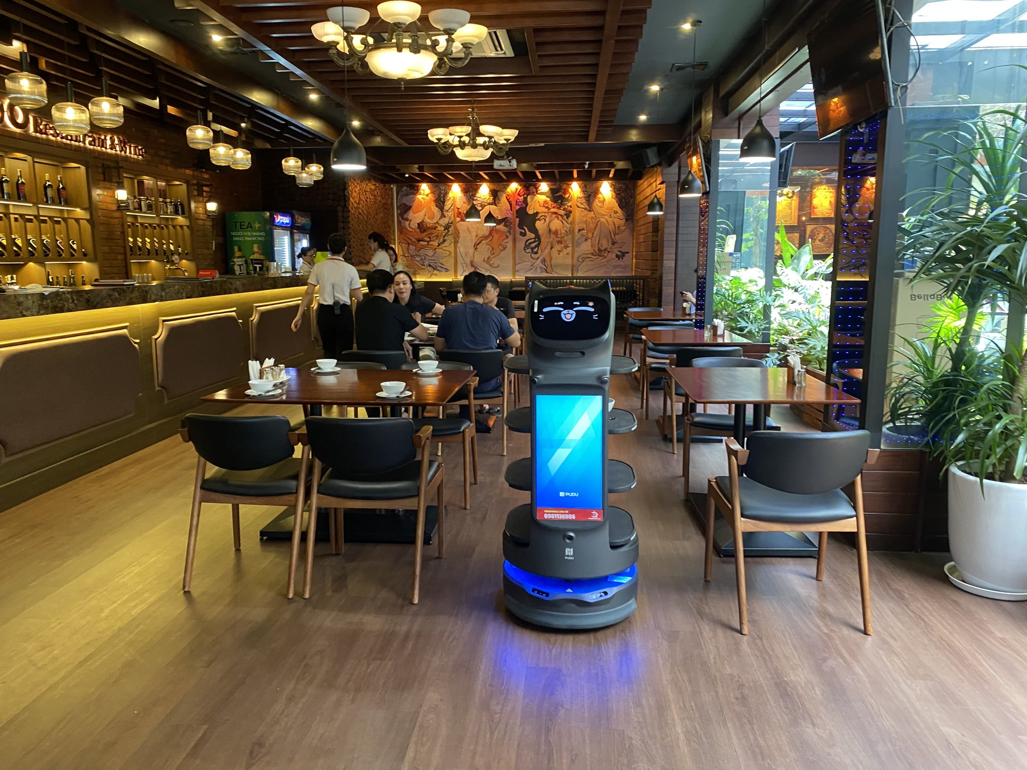Robot phục vụ BellaBot Pro di chuyển trên lối đi giữa các dãy bàn nhà hàng