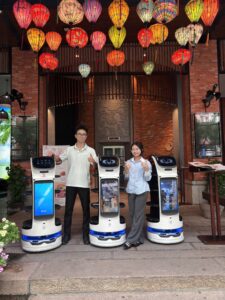 Ba robot phục vụ BellaBot Pro đứng trước lối vào một nhà hàng tại Đà Nẵng trang trí đèn lồng