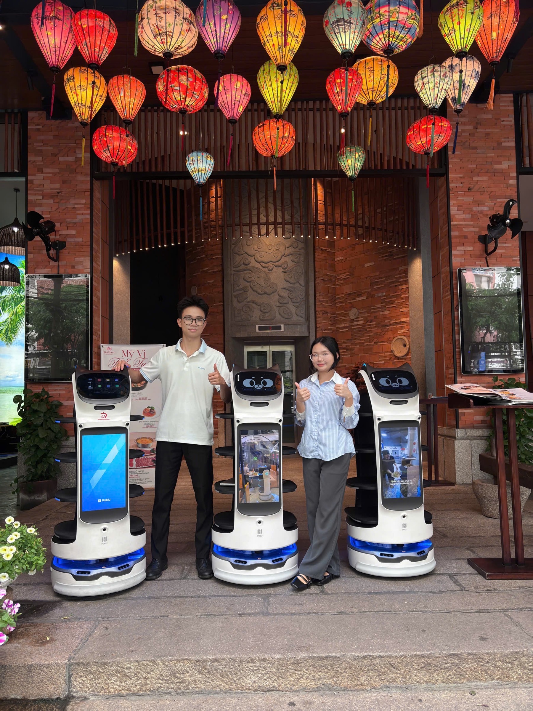 Ba robot phục vụ BellaBot Pro đứng trước lối vào một nhà hàng tại Đà Nẵng trang trí đèn lồng
